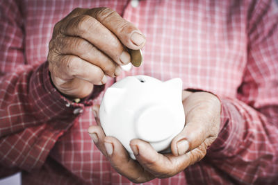 Midsection of man putting coin in piggy bank