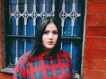 Portrait of young woman standing against window