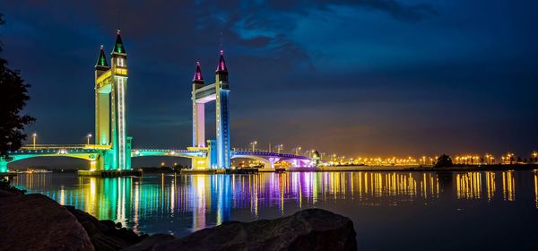 Illuminated drawbridge by river against sky at night