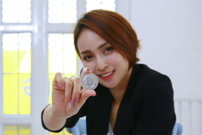 Portrait of beautiful businesswoman showing coin in office 