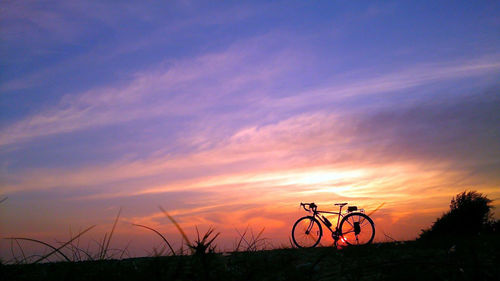 Silhouette bicycle on field against sky during sunset