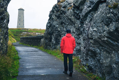 Rear view of man standing by wall against sky