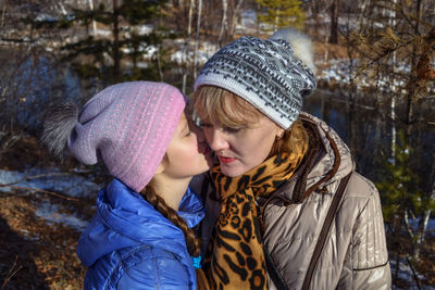 Daughter whispering in ear of mother during winter