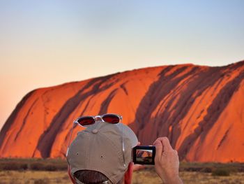 Rear view of man photographing with camera against mountains and sky