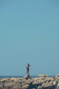 Man standing on rock against clear blue sky