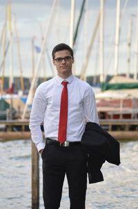 Portrait of young man standing by boat at harbor