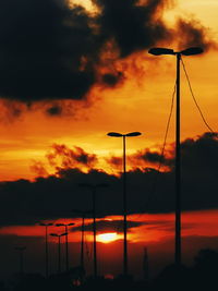 Silhouette street lights against dramatic sky during sunset