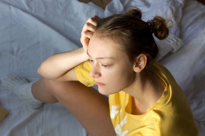 High angle view of sad teenage girl sitting on bed