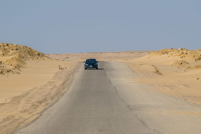 Car on road in desert against clear sky