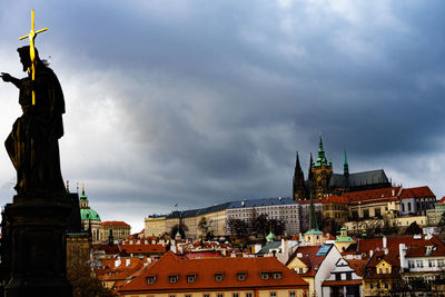 Statue of buildings in city against cloudy sky