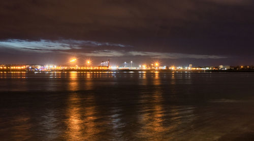 Illuminated city by sea against sky at night