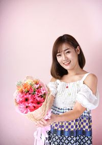 Portrait of smiling woman standing against pink wall