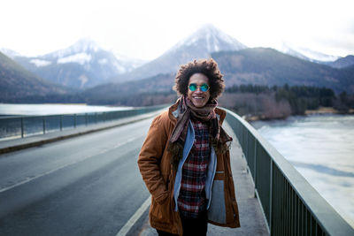 Smiling young man standing on bridge against mountains