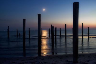 Silhouette wooden posts on beach against sky during sunset