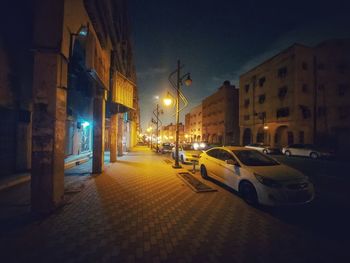 Cars on illuminated street amidst buildings at night