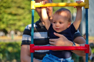 Father holding his little baby boy on playground ladder