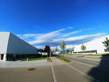 Road by buildings against blue sky