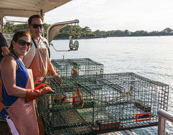 A man and a women are on a lobster boat tour ready to push off two lobster traps back in to water.