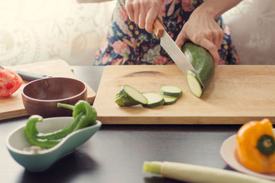 Midsection of woman cutting zucchini on cutting board
