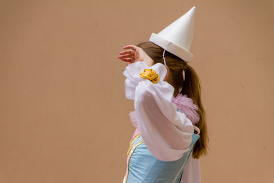 Side view of woman wearing party hat standing against beige background