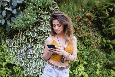 Young woman using phone while standing on plants