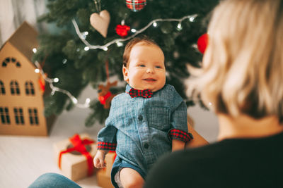 Cute smiling boy sitting against christmas tree at home