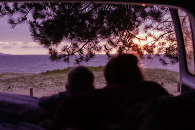 Rear view of silhouette man sitting by sea against sky