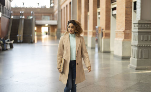 Young businesswoman holding laptop walking at station