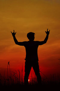 Silhouette man with arms outstretched standing on field against sky during sunset