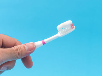 Cropped image of hand holding toothbrush against blue background