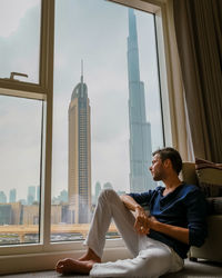 Side view of woman sitting on window