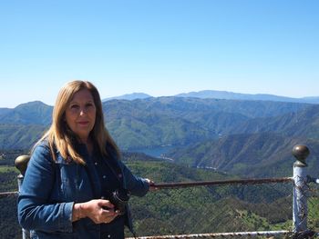 Portrait of young woman standing on mountain against clear blue sky