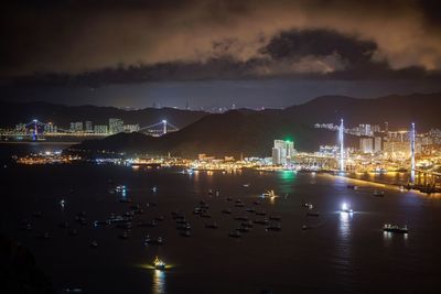 Illuminated city by sea against sky at night