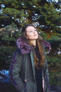 Portrait of beautiful young woman standing against trees