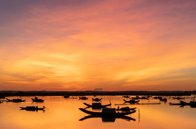 Silhouette boats in sea against orange sky