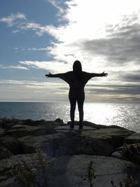 Rear view of woman standing on rock at sea shore against sky