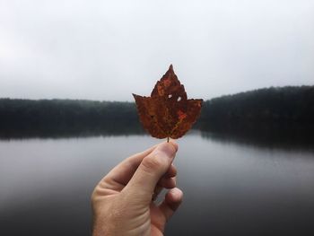 Close-up of hand holding autumn leaf against lake