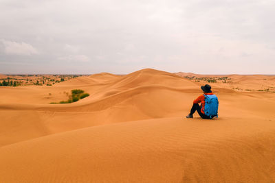 Rear view of man sitting on sand at desert