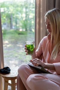 A blond woman in pink pajama sits in the pink armchair and sips mint tea.