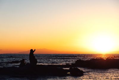 Silhouette man standing on rock against sea during sunset