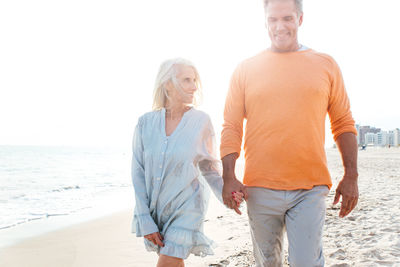 Smiling couple holding hands while walking at sandy beach