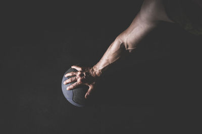 Close-up of hand holding basketball over black background