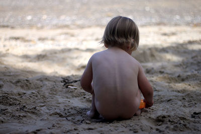 Rear view of naked baby boy playing on sand at beach