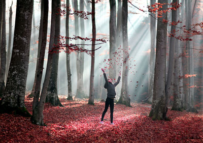 Girl throwing dry red autumn leaves in forest