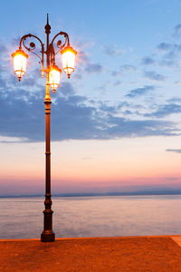 Street light by sea against sky during sunset