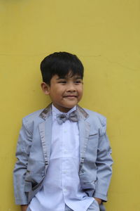 Portrait of boy standing against yellow wall