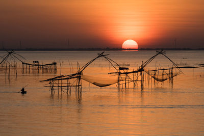 Silhouette wooden posts in sea against orange sky