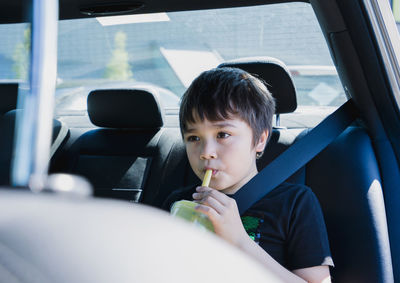 Portrait of boy sitting in car drinking cold drink