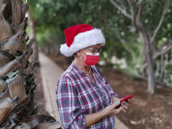Senior woman wearing mask using smart phone while standing outdoors