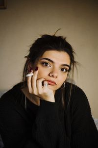 Portrait of young woman smoking cigarette against wall